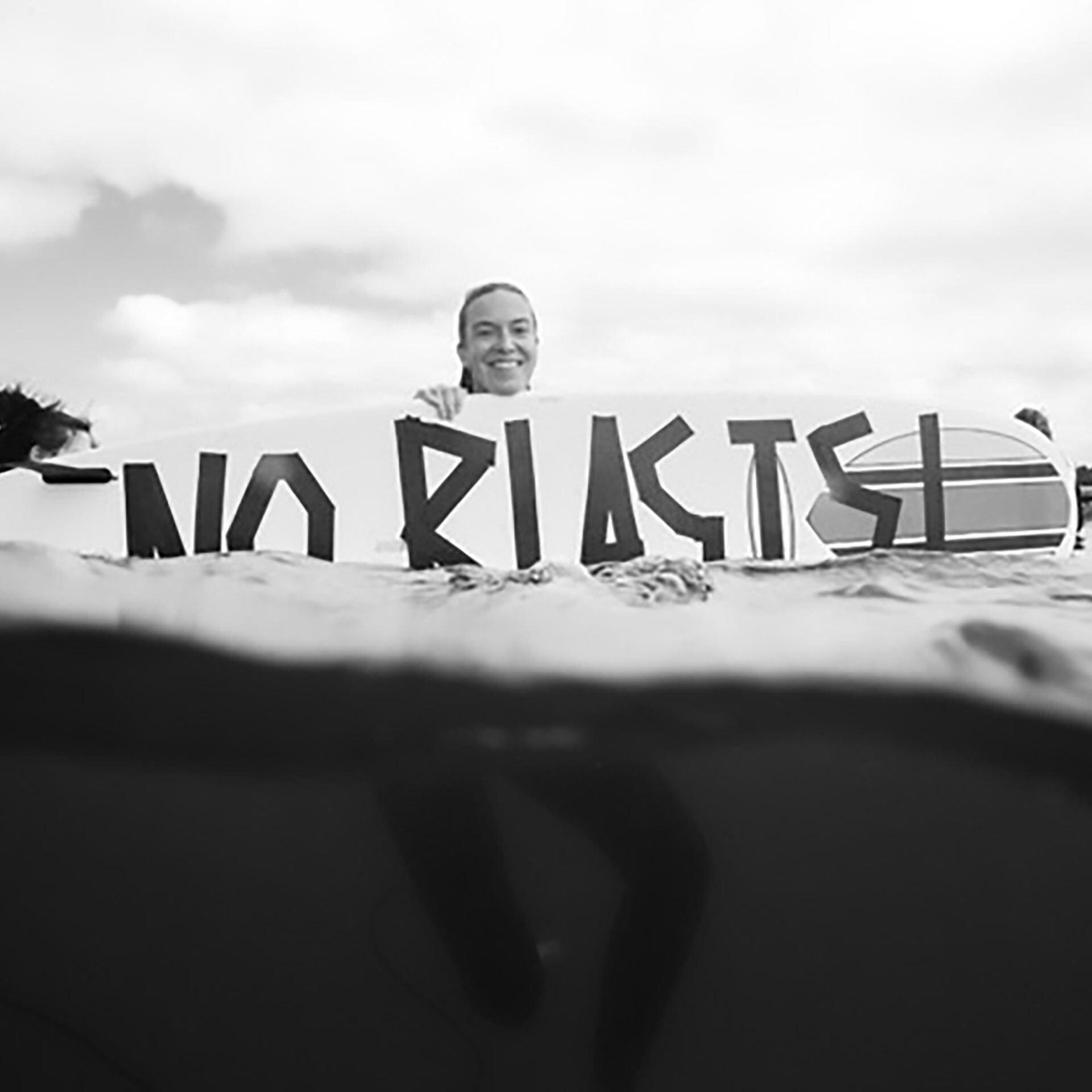 A person in the a water on a surfboard holding a sign that reads 